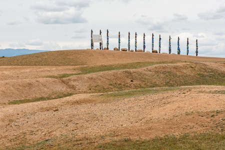 A series of serges at Shamanka on Olkhon Island. Row of 13 high ritual Buryat religious pillars tied with colored ribbons, against the background blue sky with clouds. The photo was taken in the summer in July.の写真素材