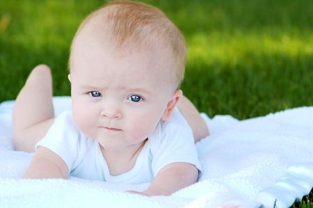 Serious baby outside on a white blanket