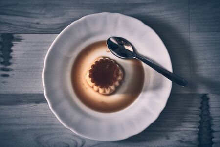 Fresh Flan dessert on a dark natural wood background from above, on a white plate with spoonの写真素材