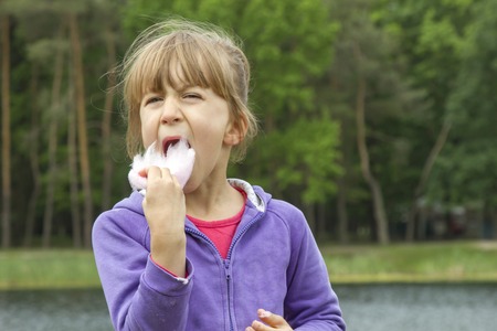 Little girl eating cotton candy in the park in springの写真素材