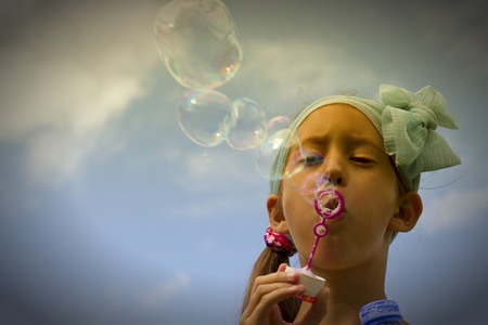 A little girl blowing soap bubbles in summer park. Backgroundの写真素材
