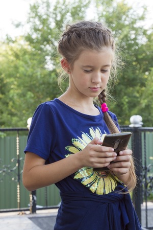 Little girl playing with a smartphone outdoors.の写真素材