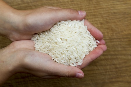 Female hands full of white rice on wooden backgroundの写真素材