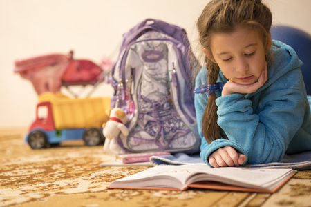 Child reading book at home. Girl doing homeworkの写真素材