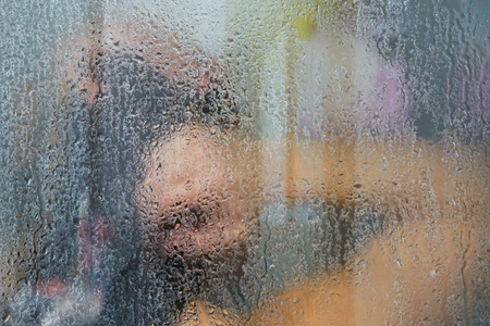 Woman washing behind weeping glass shower door