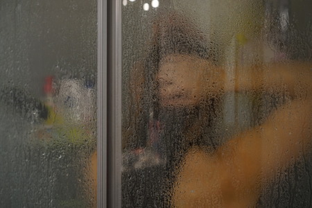 Woman washing behind weeping glass shower doorの写真素材