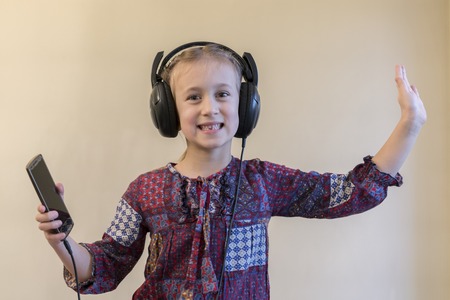 little girl listens to music on a smartphone and dances
