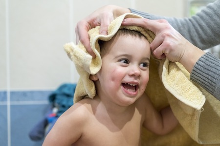 Mom wipes the towel of a funny baby boy. The kid laughs and rejoices
