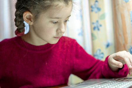8 year old girl with a pigtail in a red sweater working on a laptopの写真素材