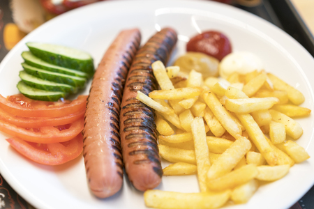 Grilled sausages with chips and vegetables on a white plate. harmful food concept.の写真素材