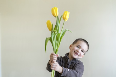 Boy hiding flower on his hands. Light background. European appearanceの写真素材