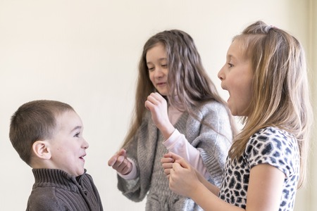 Two little girls beat the boy. Light background. European appearanceの写真素材