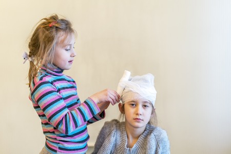 Two girls play doctor. Bandage your head with a bandage.