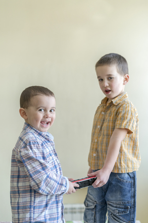 The boy shares a toy with a friend. Two cheerful little boys. Two brothers. Boys in plaid shirtsの写真素材