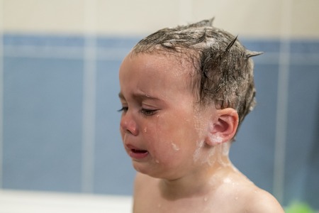 Crying baby by in a bathtub. Infant kid sreaming while taking a bath. baby cries in the bathroomの写真素材