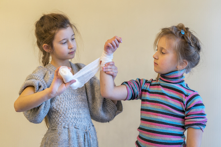 The girl bending her sister's hand. Two, girls, play, doctor. Bandage your arm with a bandage. Hand injury. First aid.の写真素材