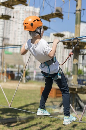 Little beautiful girl climbs on rope harness in summer city parkの写真素材