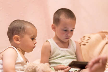 children in the bedroom watching cartoons. children play on smarfone. two brothers in the bedroom...