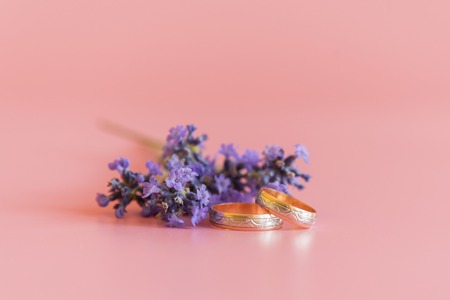Wedding rings and lavender flowers on a pink background.の写真素材