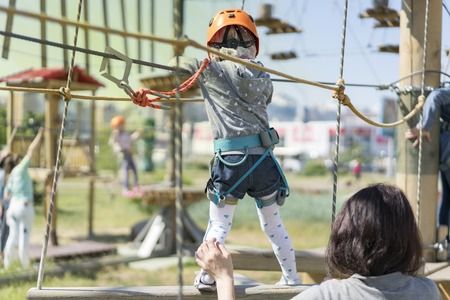 Little beautiful girl climbs on rope harness in summer city parkの写真素材