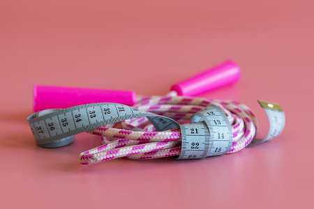 Sports and health idea. Workout and refreshment concept. Tape around jump rope and barbells on yoga mat. Skipping rope, dumbbells in cyan color tied with measuring tape on pink background.の写真素材