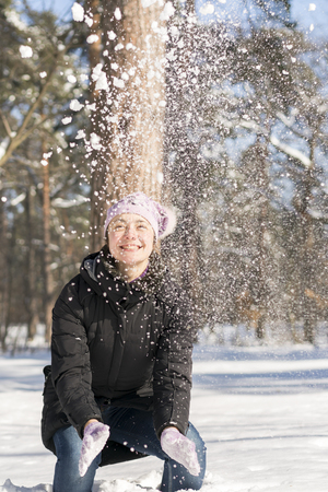 Girl throws snow up. Portrait of the beautiful girl throwing snow in the winter. Happy young woman plays with a snow in sunny winter day. vertical photo.の写真素材