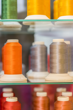 Background with a lot of colorful coils with threads. Bobbins are stacked in three rows, one on the...