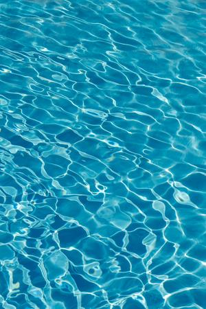 Blue water in swimming pool background. Ripple Water in swimming pool with sun reflection. Blue swimming pool rippled water detail. vertical photo.の写真素材