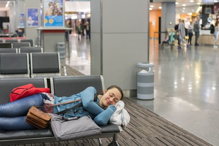 Young woman sleeping at the airport while waiting for her flight. Tired female traveler sleeping on the airpot departure gates bench with all her luggage by her side. Tireing travel concept.の写真素材