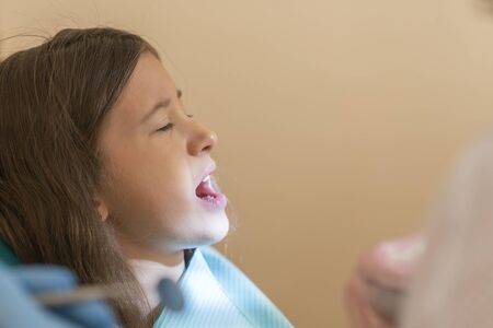 Little girl at the reception in the dentist's office. little girl sitting in a chair near a dentist after dental treatment. Little girl sitts in the dentist's officeの写真素材