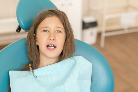 Little girl at the reception in the dentist's office. little girl sitting in a chair near a dentist after dental treatment. Little girl sitts in the dentist's office.の写真素材