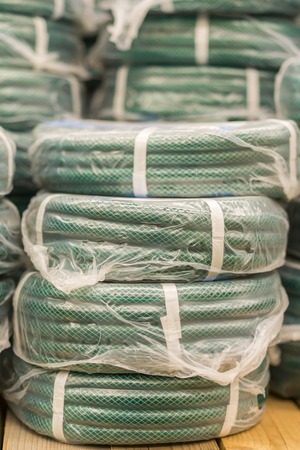 stacks of rolls yellow pvc plastic pipe on the counter in the store. Sale Hoses in the garden of various manufacturers, on shelves in store. Hose for watering in the store. vertical photoの写真素材