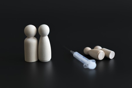 child vaccination concept. Failure of vaccines leads to death. wooden figures of parents of children and a syringe on a black backgroundの写真素材