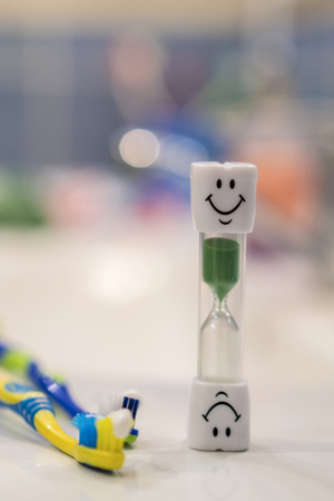 Concept of recommended time to brush your teeth. Soft focus. Two toothbrushes and hourglass. Brushing teeth for 3 Minutes. vertical photo.の写真素材