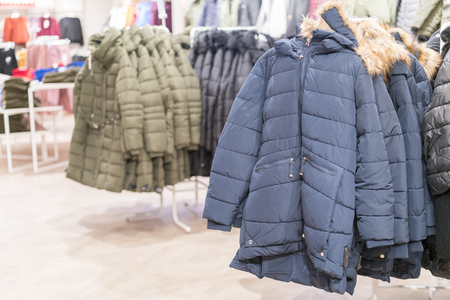Set of clothes, coat on the rack clothing shop interior on background. Winter jackets in a store.の写真素材