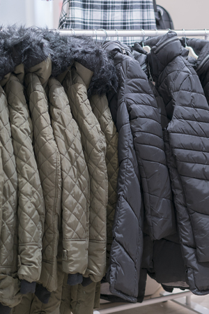 Set of clothes, coat on the rack clothing shop interior on background. Winter jackets in a store. vertical photo.の写真素材