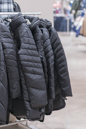 Set of clothes, coat on the rack clothing shop interior on background. Winter jackets in a store. vertical photoの写真素材