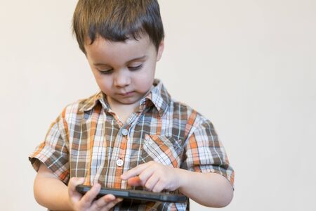 Portrait of a smiling little boy holding mobile phone isolated over light background. cute kid...