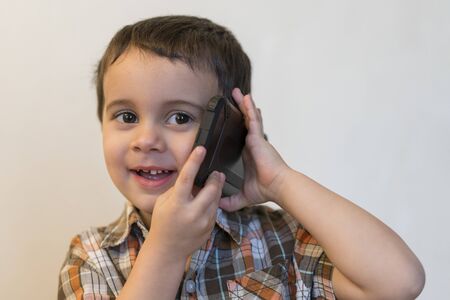 Cute little boy talking by mobile phone on light background. Happy little boy standing and talking...