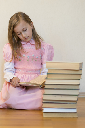 Girl reading a book sitting on the floor in an apartment. Cute girl reading book at home. education and school concept - little student girl sitting on floor and reading book. vertical photoの写真素材