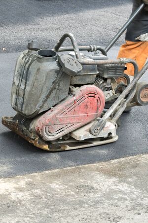 Road workers compact the asphalt with a vibrating rammer on the road. Worker with compactor at a...