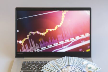 Dollar bills laying on a laptop with bitcoin charts on a blurred background.の写真素材