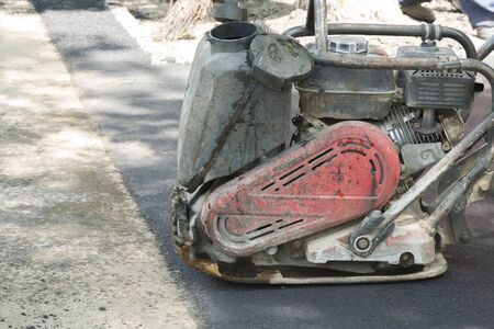 Road workers compact the asphalt with a vibrating rammer on the road. Worker with compactor at a road construction siteの写真素材