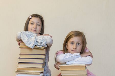 Two sisters with a pile of books on the floor in the room. The concept of education and development of children. Love of literature.の写真素材