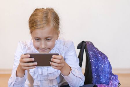 School girl plays on the smartphone. Kid play game, surfing online, learning...etc. Mockup. vertical photo. Back to School.の写真素材