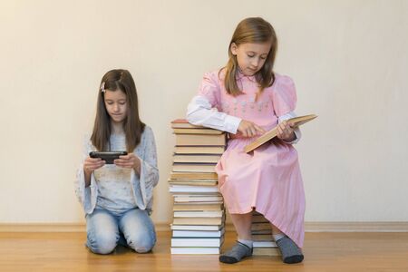 Two sisters with a pile of books on the floor in the room. The concept of education and development of children. Love of literatureの写真素材