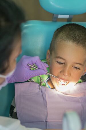 Pediatric dentist examining a little boys teeth in the dentists chair at the dental clinic. A child with a dentist in a dental office. Close up of dentist examination little boy's teeth in clinic. vertical photo.の写真素材