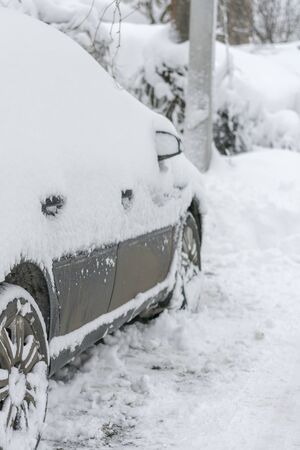 Snow-covered machine. Car under the snow. Lots of snow and big snowdrifts on the street. Vehicles are completely covered in snow. Cold winter weather. vertical photo.の写真素材
