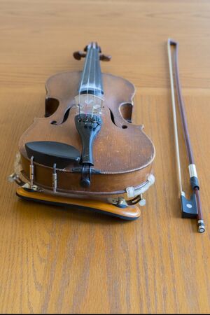 violin lying on a wooden textured table. Violin body and bow on wood table with golden glow. Top view. Horizontal composition. vertical photo.の写真素材