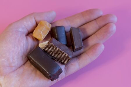 Hand with chocolates on a pink background. Enjoying sweets. Sweet addiction concept. The concept of...